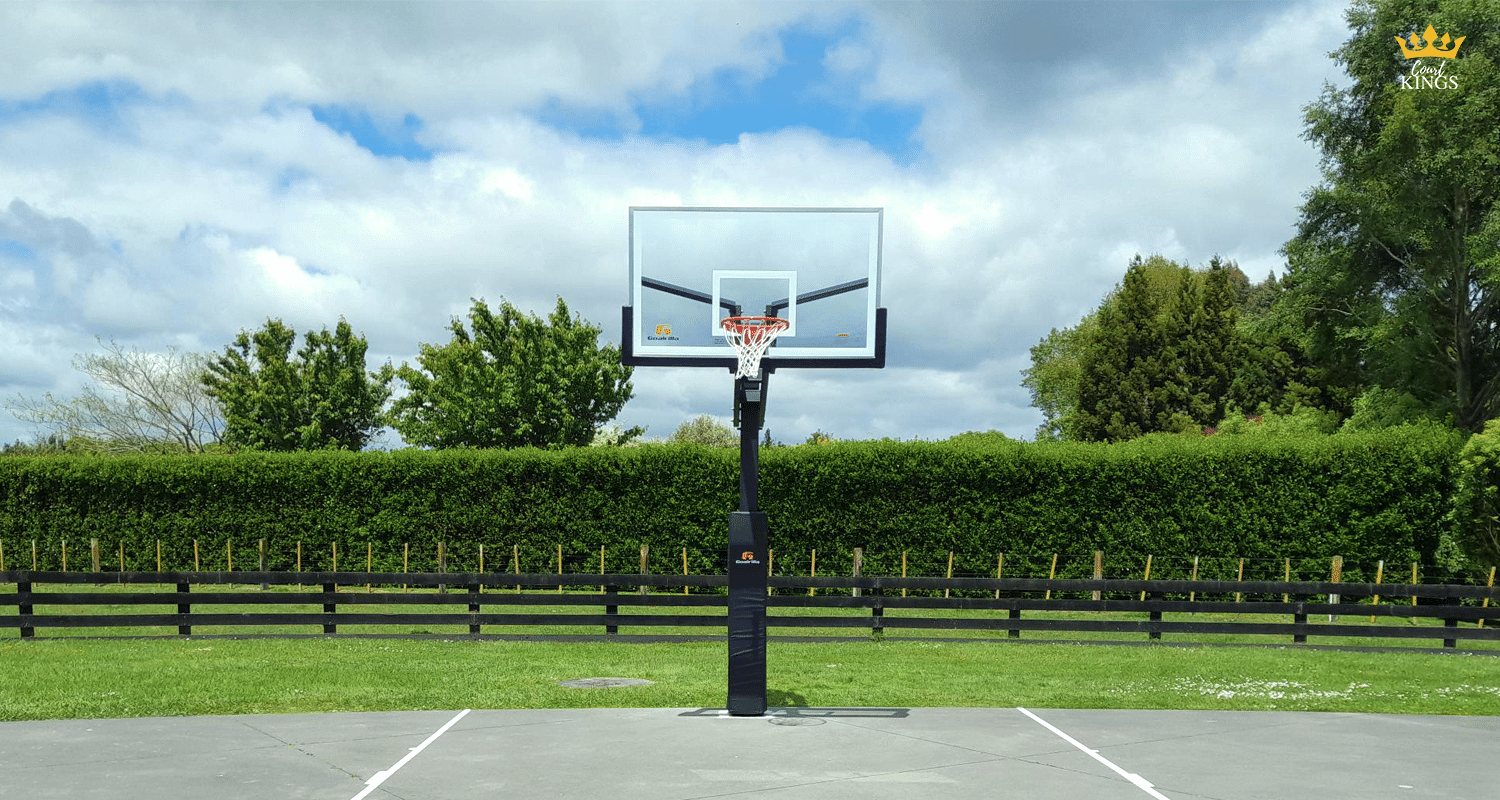 Outdoor basketball hoop with glass backboard on a concrete court in a backyard setting