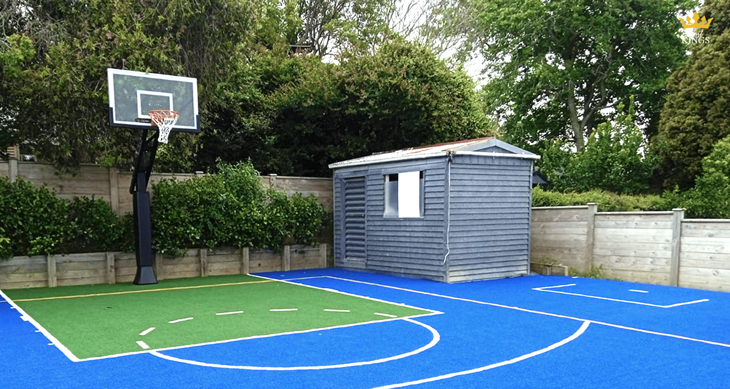 Outdoor basketball hoop next to a blue and green backyard court with a small shed and timber fence