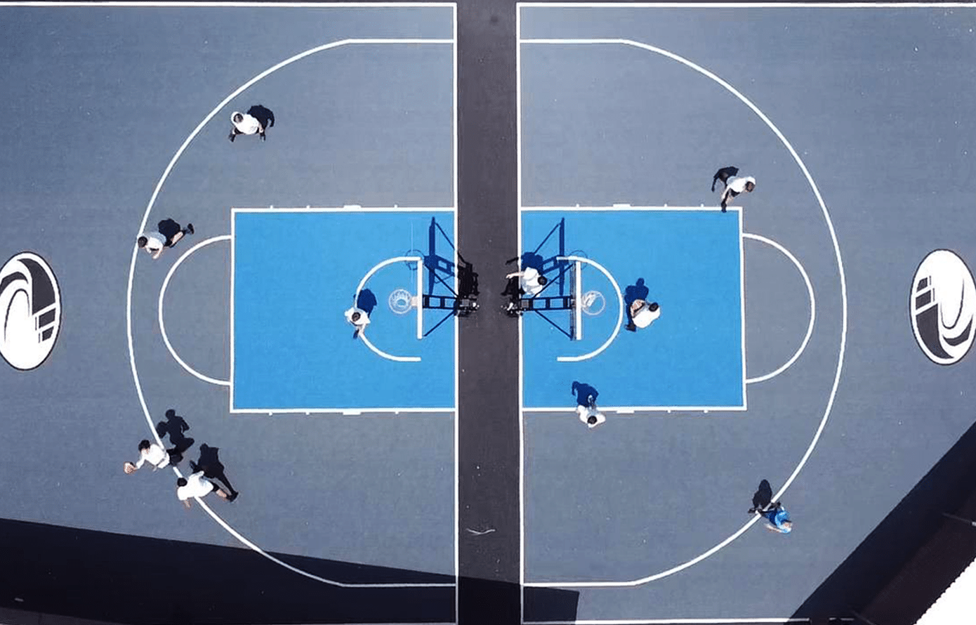 A professional in-ground basketball hoop with a clear glass backboard, installed by Court Kings on a custom purple and grey outdoor court in a New Zealand park.