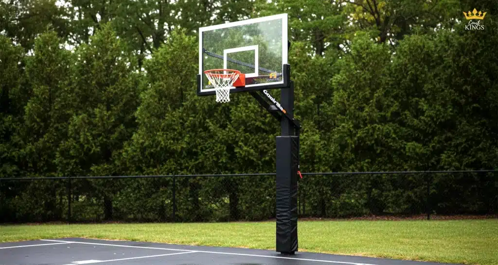 What is the best material for an outdoor basketball hoop on a backyard court Outdoor basketball hoop with a tempered glass backboard and powder-coated steel pole and rim on an asphalt court beside a hedge.